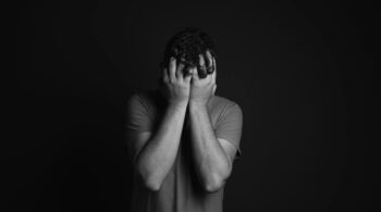 gray scale photo of man covering face with his hands