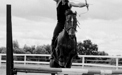 grayscale photo of man shooting an arrow while riding a horse